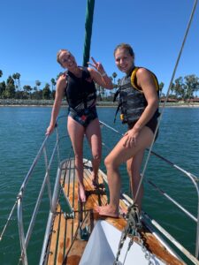 Two females standing on the Bow Sprit of the sailboat, enjoying the Swimming Adventure at the private cove.
