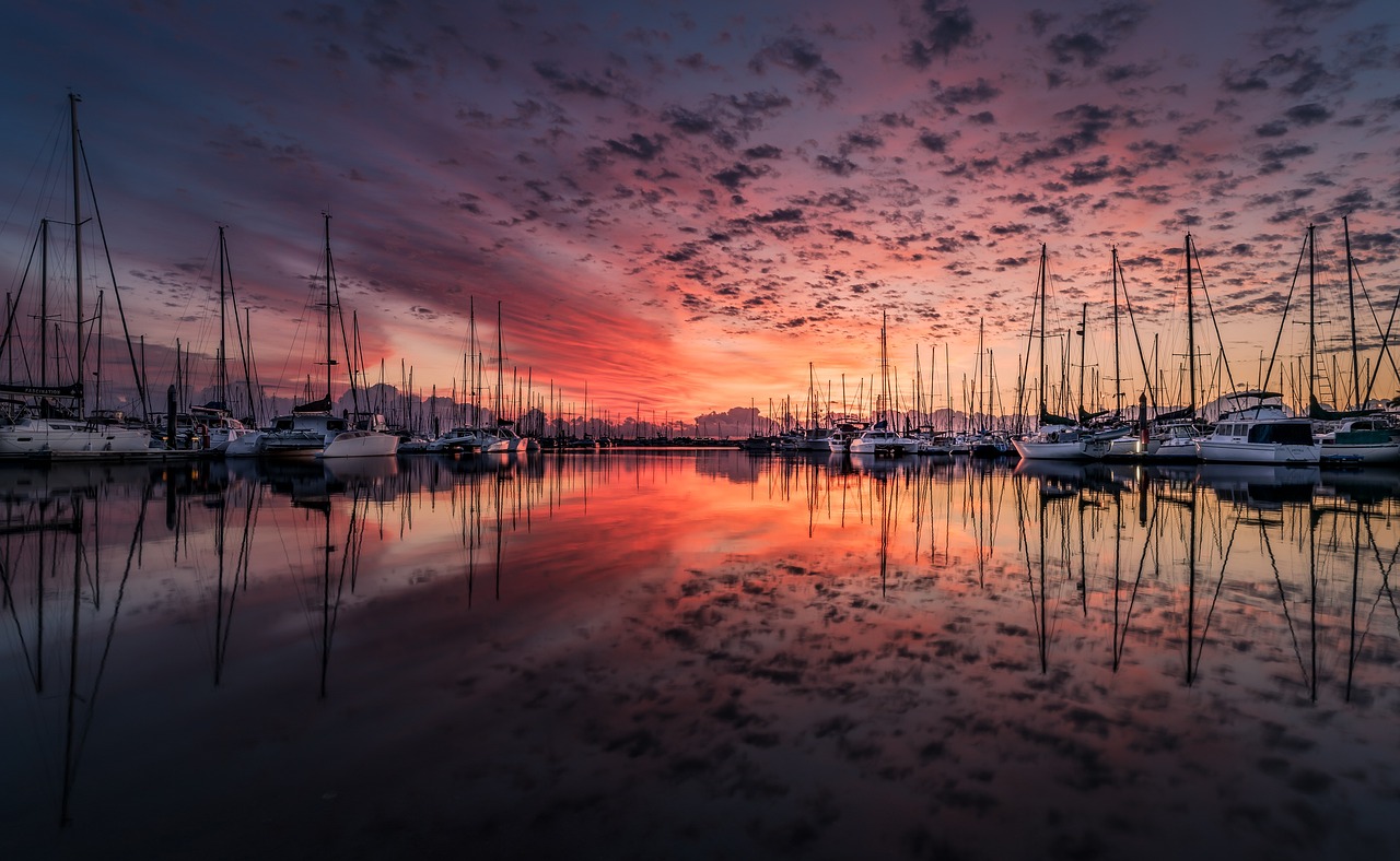 A magnificent sunrise mirrored off tranquil waters of the marina lined with sailboats.