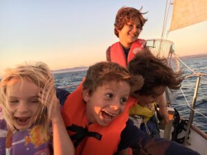 Closeup of children joyously laughing at the Bow of the boat, while under sail.